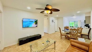 A modern living room with a flat-screen TV, a glass coffee table, and a ceiling fan. - Near Fort Myers Beach • 2BR • 2BA • Grill (Fort Myers Beach)