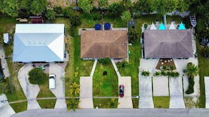 An aerial view of a residential area with three houses, each with distinct roof shapes and surrounded by greenery. - Near Fort Myers Beach • 2BR • 2BA • Grill (Fort Myers Beach)