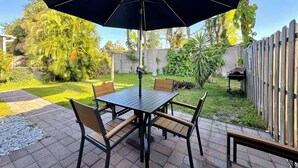 An outdoor patio with a table and chairs, a large umbrella, and a wooden fence. - Near Fort Myers Beach • 2BR • 2BA • Grill (Fort Myers Beach)