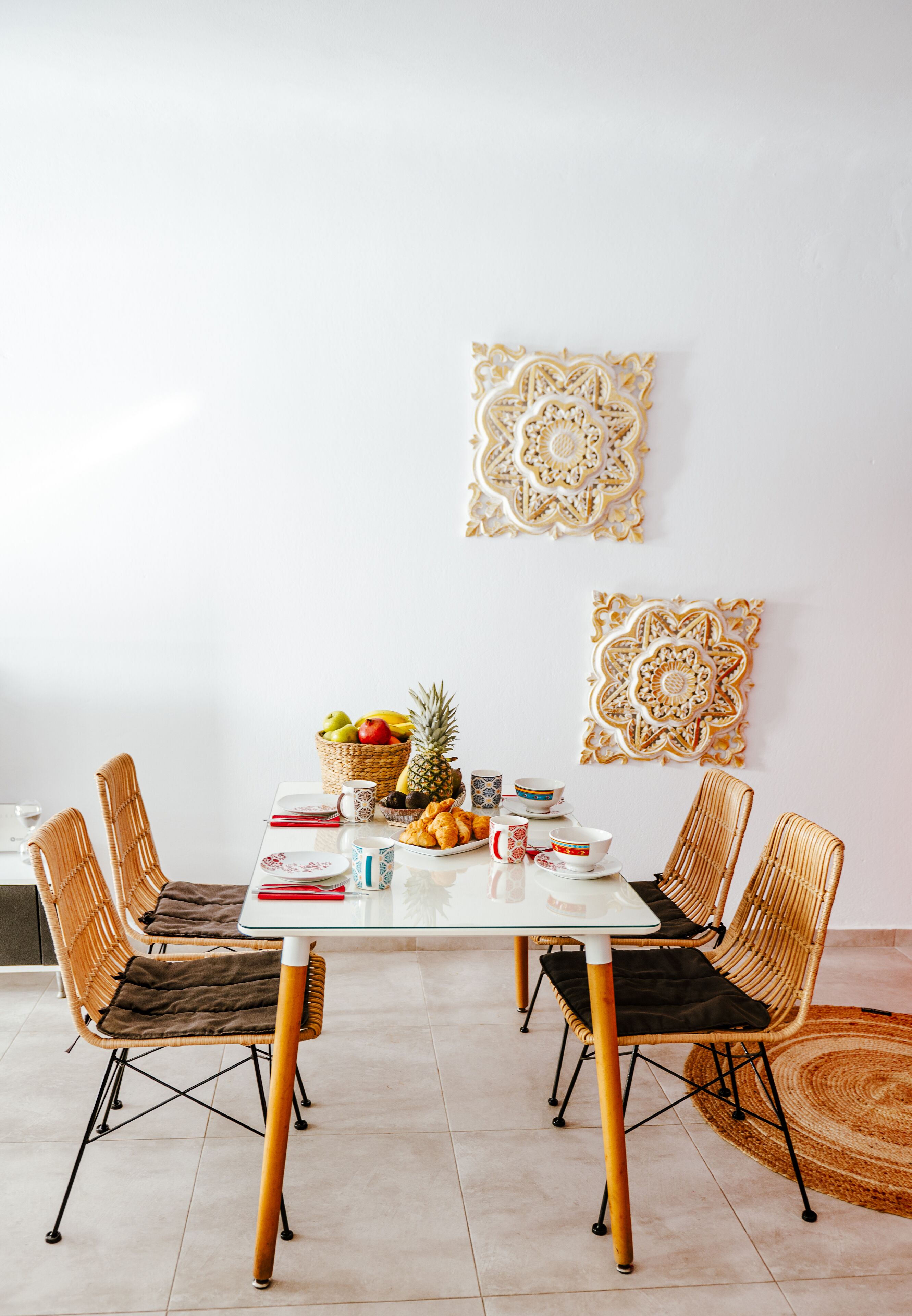 A dining area with a white table, wicker chairs, a fruit basket, and decorative wall art.