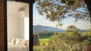 A bedroom with a bed, an air conditioning unit, and a view of a green landscape with trees and hills.