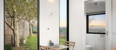 Una cocina moderna con vista a un árbol y una cerca, una mesa de madera con sillas y una ventana que da al campo.