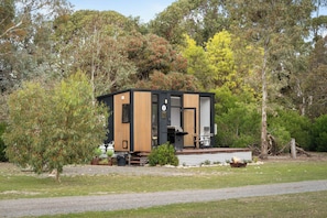 A modern, compact cabin with a wooden exterior, a small deck, and a seating area.