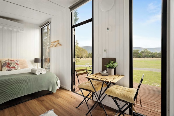 A bedroom with a bed, a table with chairs, a view of the outdoors, and a window.