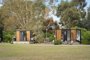 Two modern cabins with wooden exteriors, outdoor seating, and surrounded by trees.