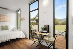 A bedroom with a bed, a desk, a chair, and a view of the outdoors.