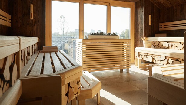 A wooden cabin with a large window, wooden benches, and a table with logs.