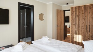 A hotel room with two beds, a shower, a wooden wardrobe, and a round mirror on the wall.