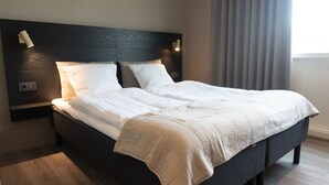 Una cama bien hecha con sábanas blancas, un cabecero oscuro y dos lámparas de noche.