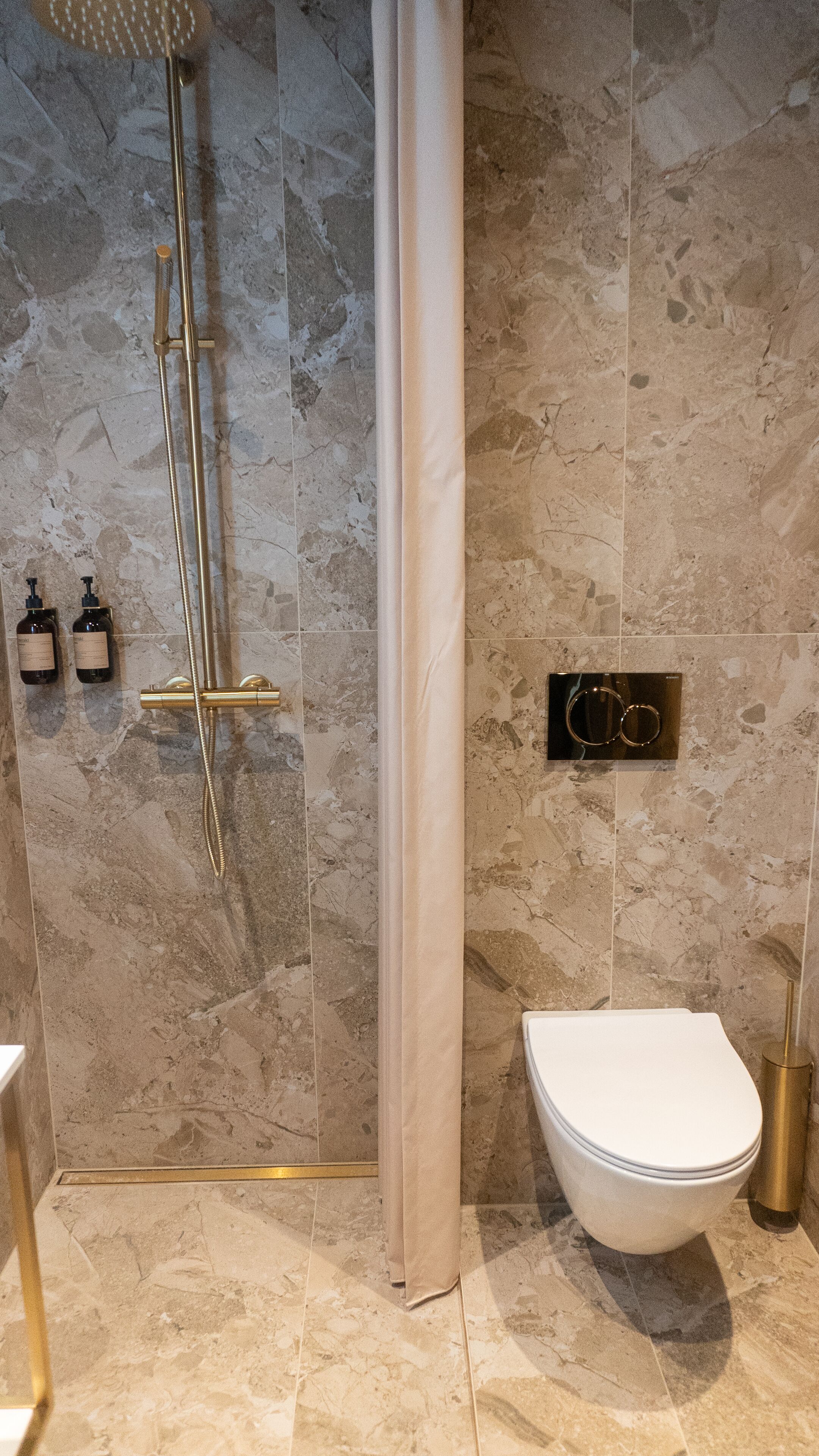 A bathroom with a shower, toilet, and two bottles of shampoo on the wall.