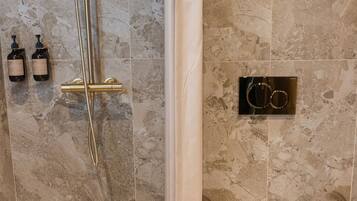 A bathroom with a shower, toilet, and two bottles of shampoo on the wall.