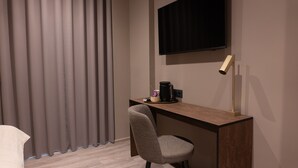 Una habitación de hotel con escritorio, silla, televisor y cortinas.