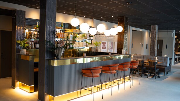 Un área de bar moderna con mostrador, taburetes y una variedad de botellas y vasos.