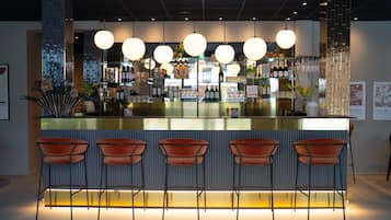 Zona de bar con mostrador de vidrio, varias botellas de alcohol y varias lámparas colgantes redondas.