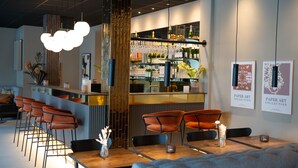 Una zona de bar con mostrador, taburetes y una exhibición de botellas y vasos.