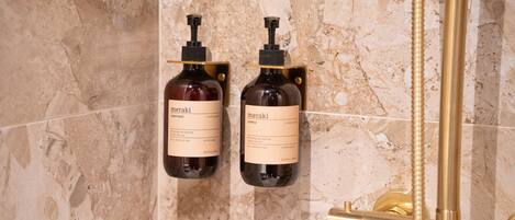 Two bottles of Meraki conditioner and shampoo hanging on a tiled wall.