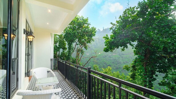 A balcony with a glass railing, white wicker furniture, and a patterned floor. - Marten's Wilderness Retreat (Lansdowne)