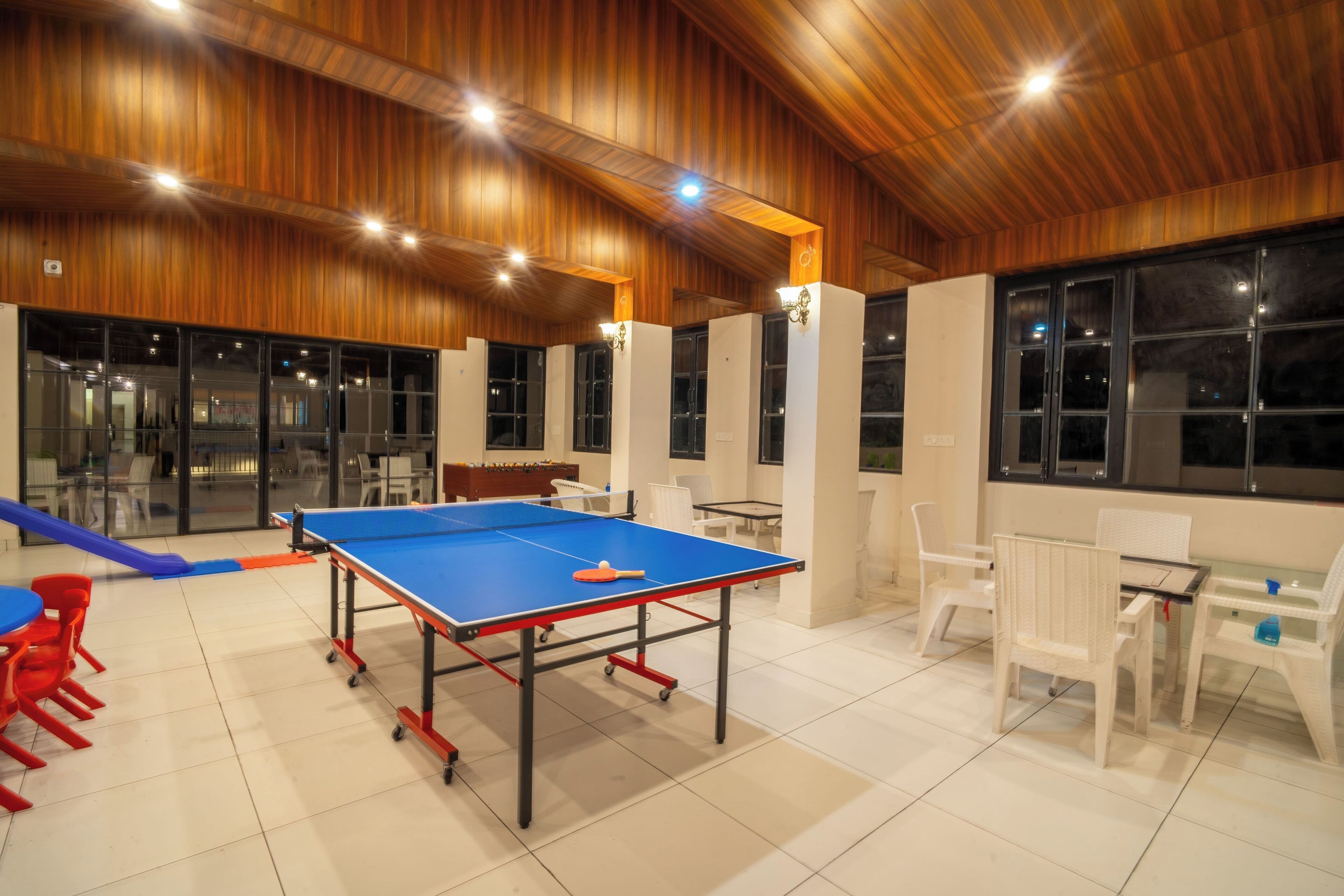 A ping pong table in a room with wooden ceiling and large windows.
