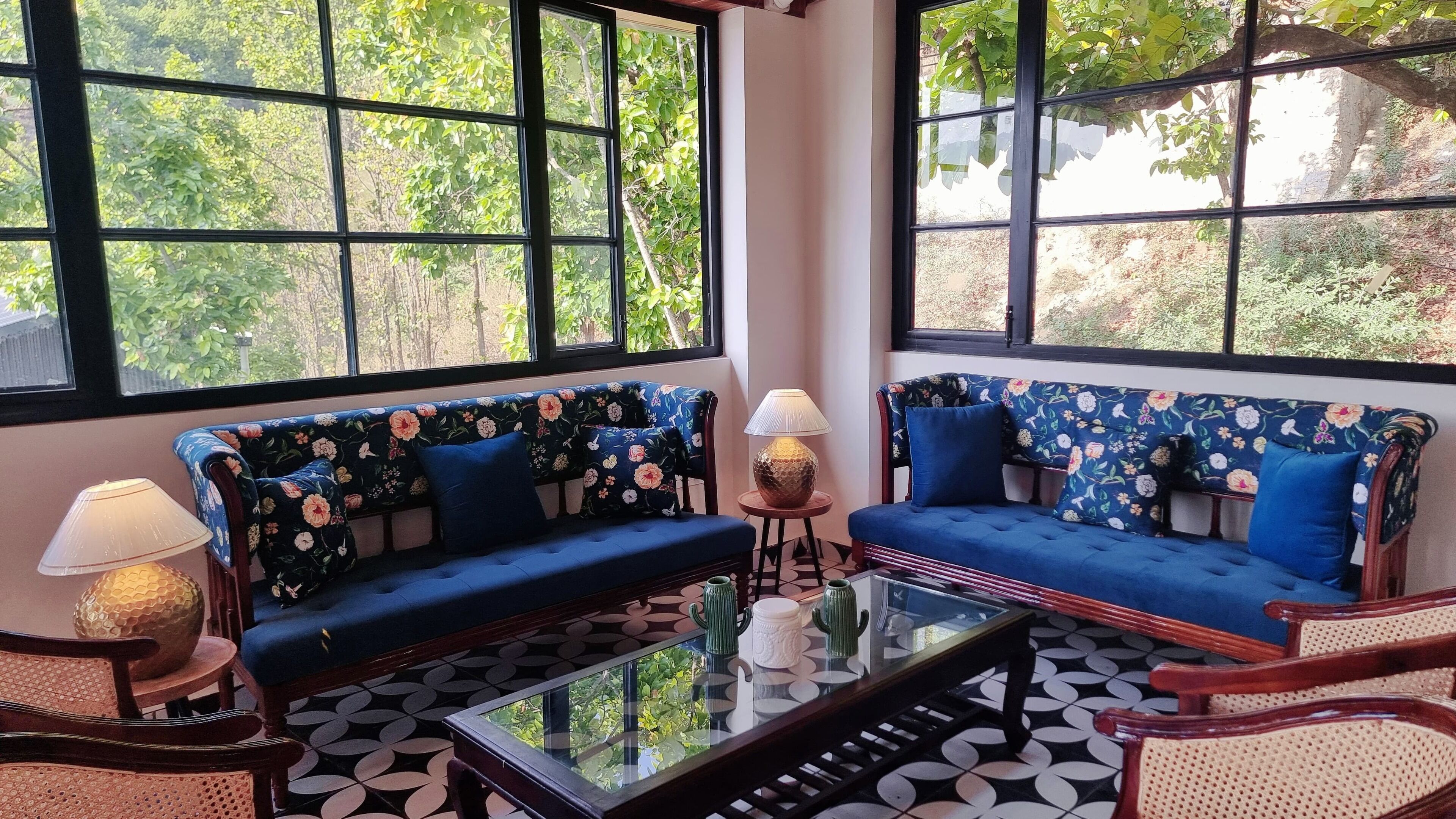 A room with two blue floral sofas, a glass coffee table, and a lamp.