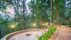 A stone pathway leading through a forested area with a circular seating area and a lantern post. - Marten's Wilderness Retreat (Lansdowne)