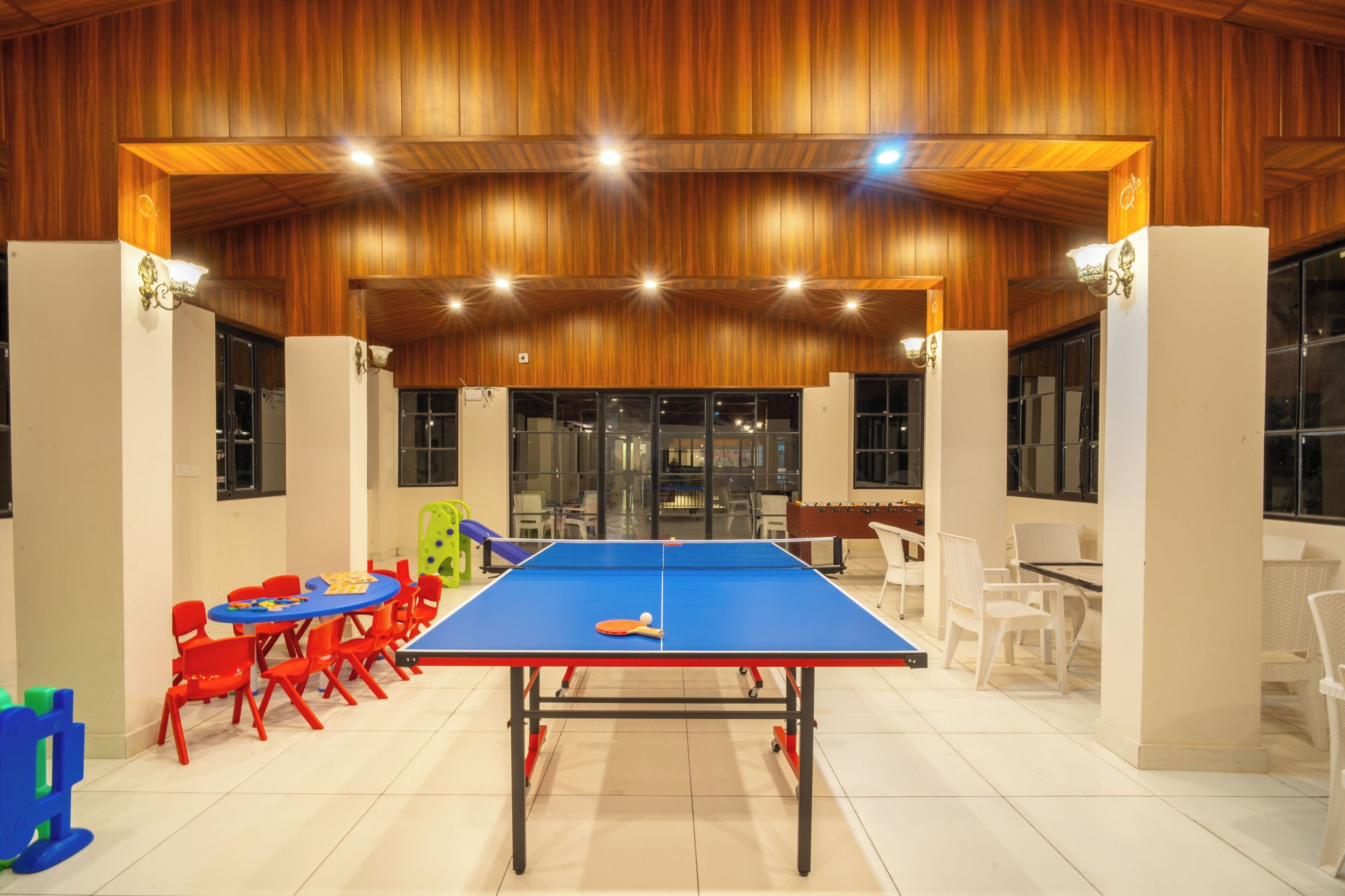 Une table de ping-pong dans une pièce dont le plafond est en bois et les murs sont blancs, entourée de chaises rouges et blanches.