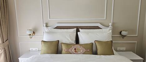 Een net opgemaakt bed met witte lakens en een groene quilt, met aan weerszijden wandlampen en vogelschilderijen erboven.