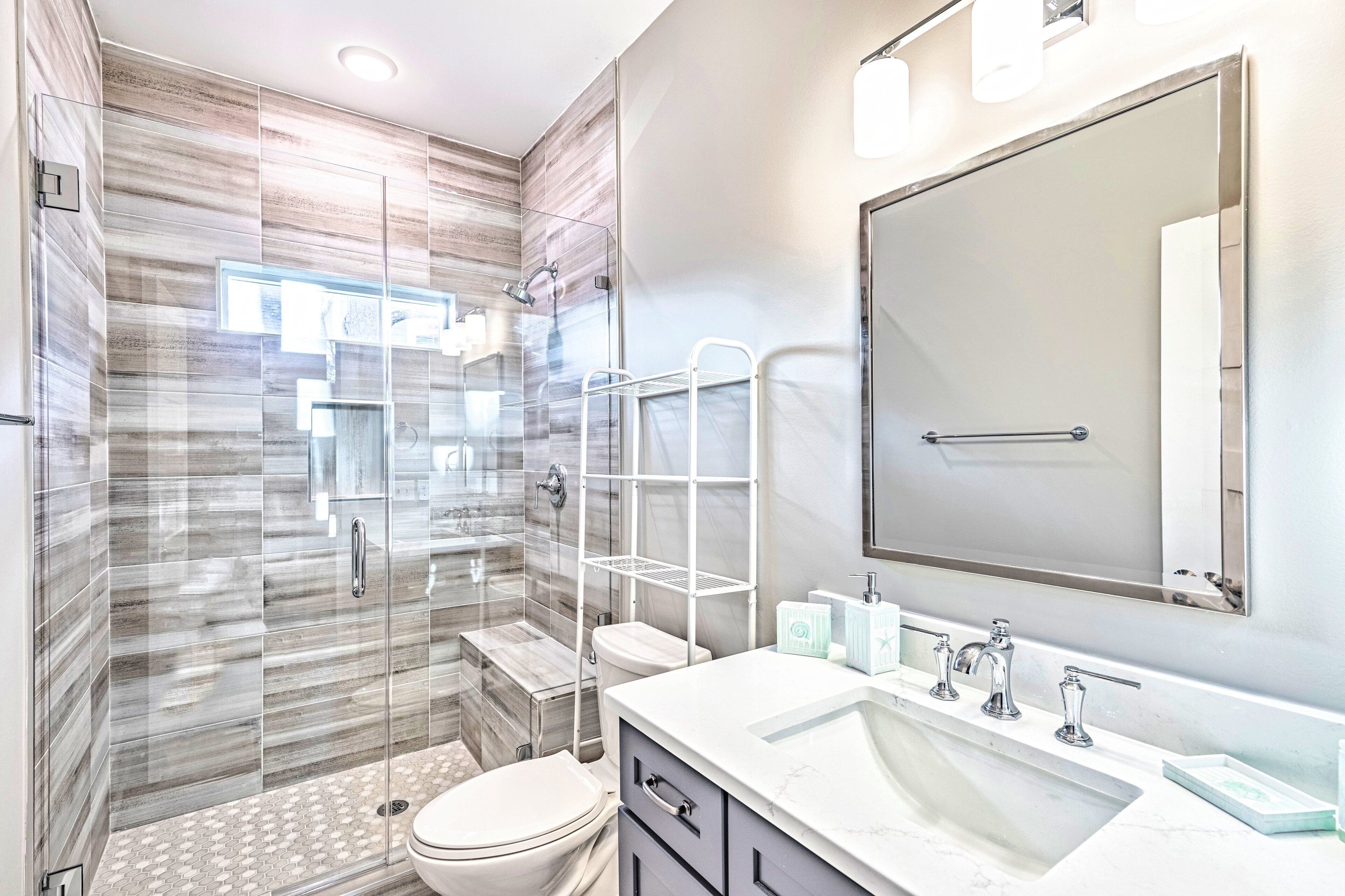 A modern bathroom with a glass-enclosed shower, a large mirror, and a white sink with multiple faucets.