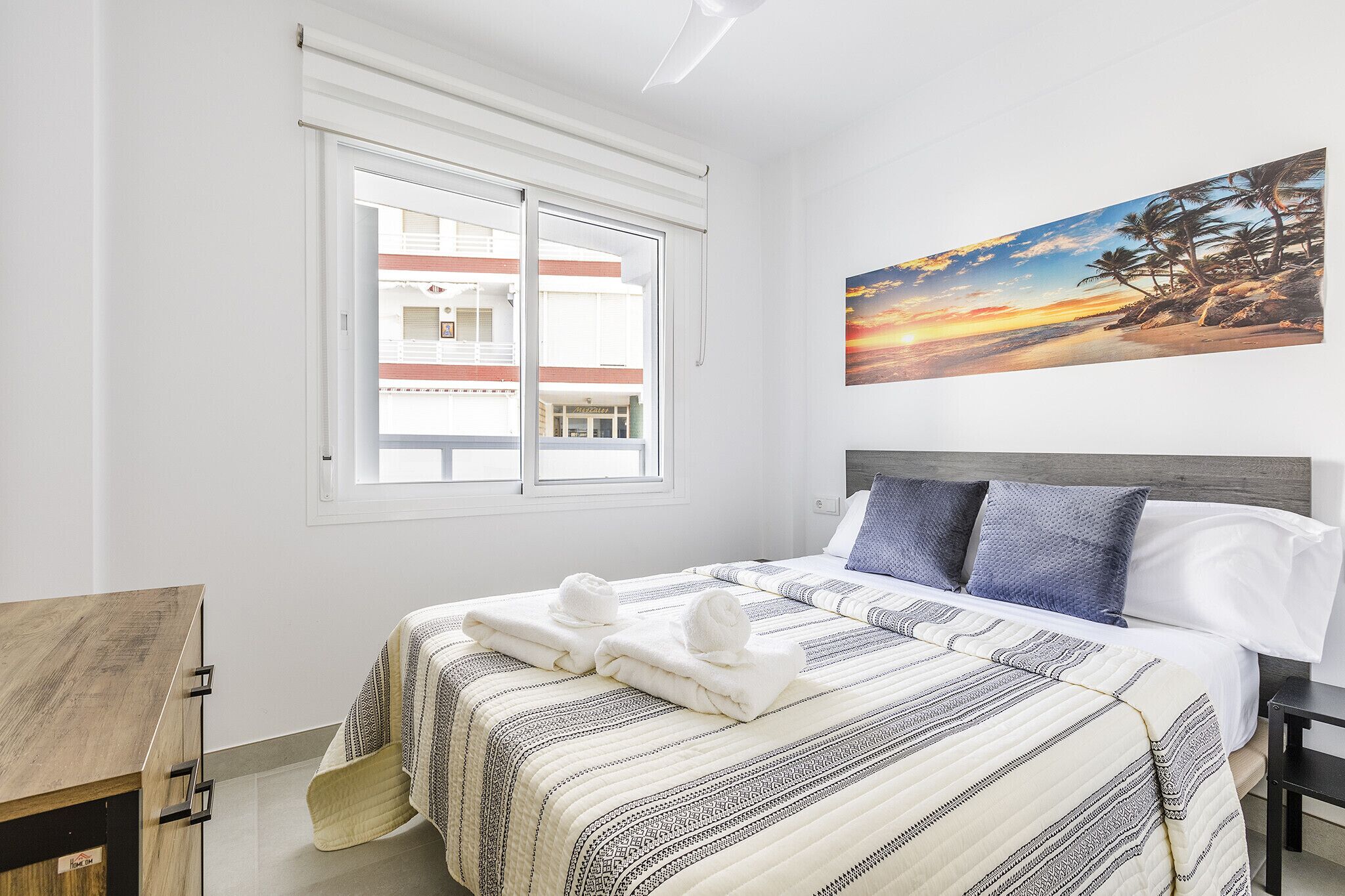 Una habitación de hotel con una cama, una ventana, un cuadro y un escritorio de madera.