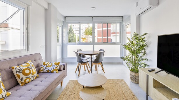 Una sala de estar moderna con sofá, mesa de centro, mesa de comedor, sillas y televisor.