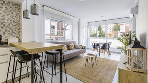 Una cocina moderna con una mesa de madera, taburetes negros, un sofá gris y una pequeña mesa redonda con sillas.