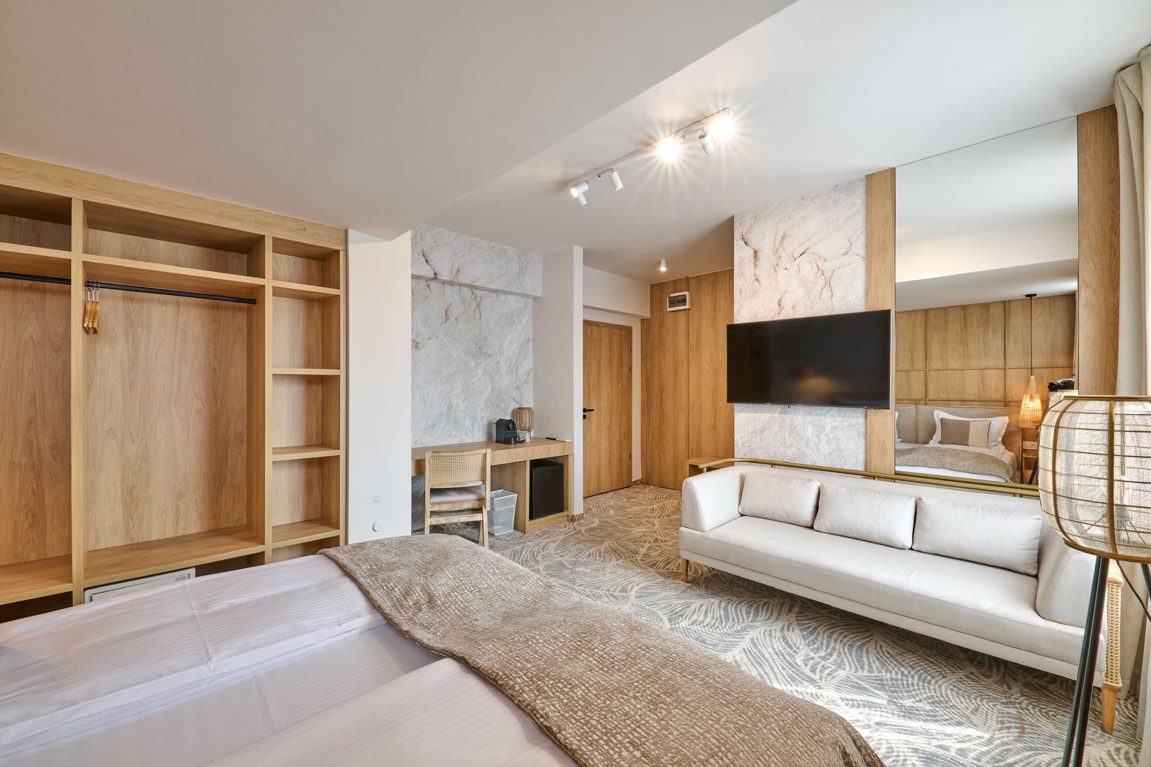Une chambre d’hôtel moderne dotée d’une grande armoire, d’un canapé, d’une télévision à écran plat et d’un bureau avec une chaise.