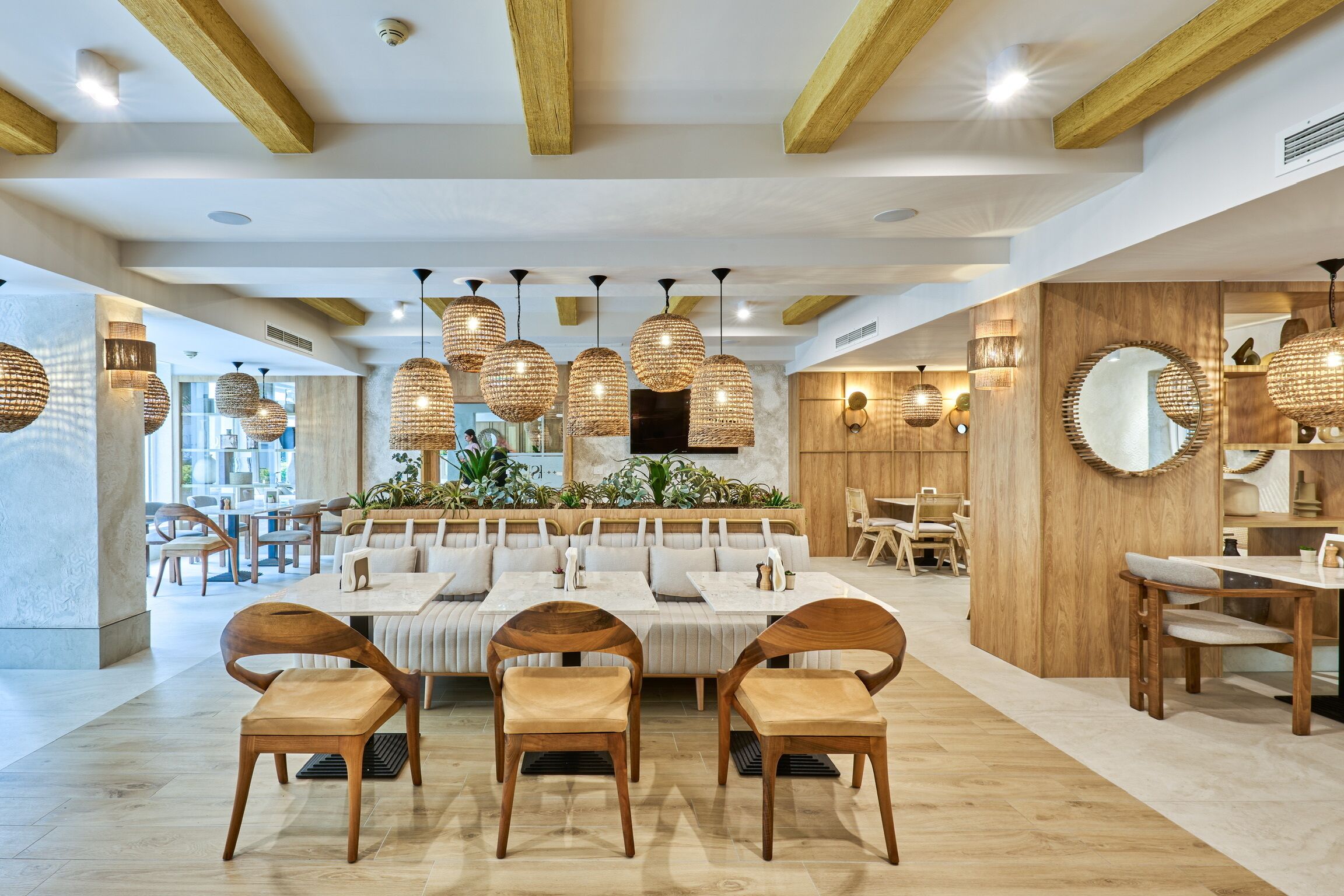 Un restaurant spacieux, doté de meubles en bois, de lustres en osier suspendus et d’un espace salon central.