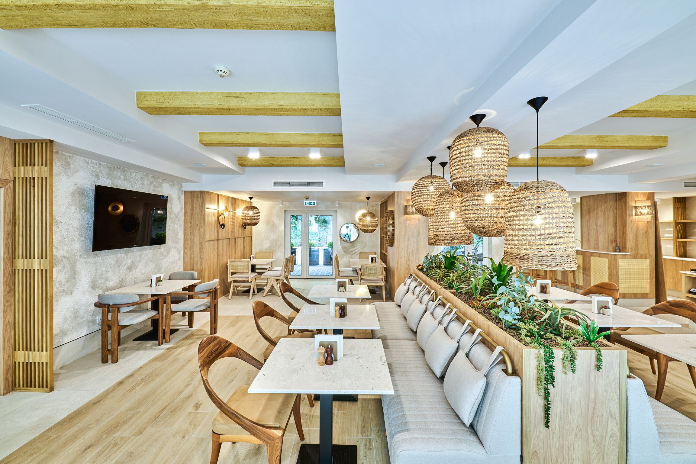 A modern restaurant interior with wooden beams, white tables, and a long bench with plants.