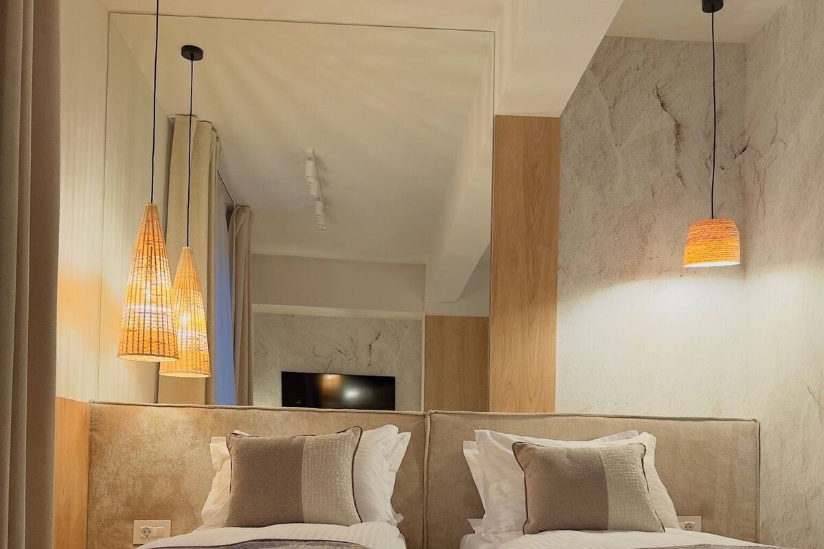 A hotel room with two beds, a flat-screen TV, and a modern chandelier.