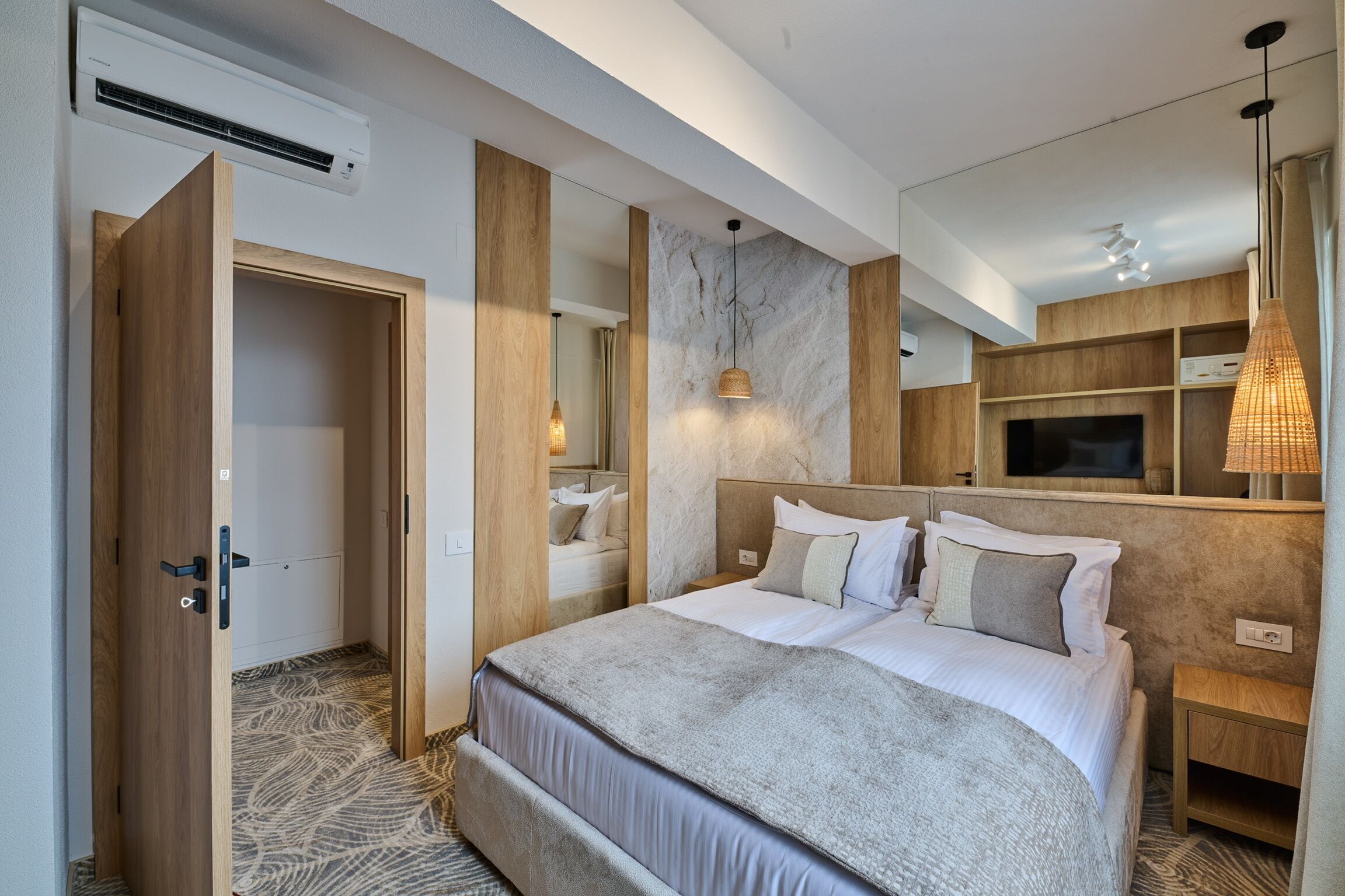 Ein modernes Hotelzimmer mit einem großen Bett, Holzvertäfelung, einer Wand aus Marmor, einem Fernseher und einer Pendelleuchte.