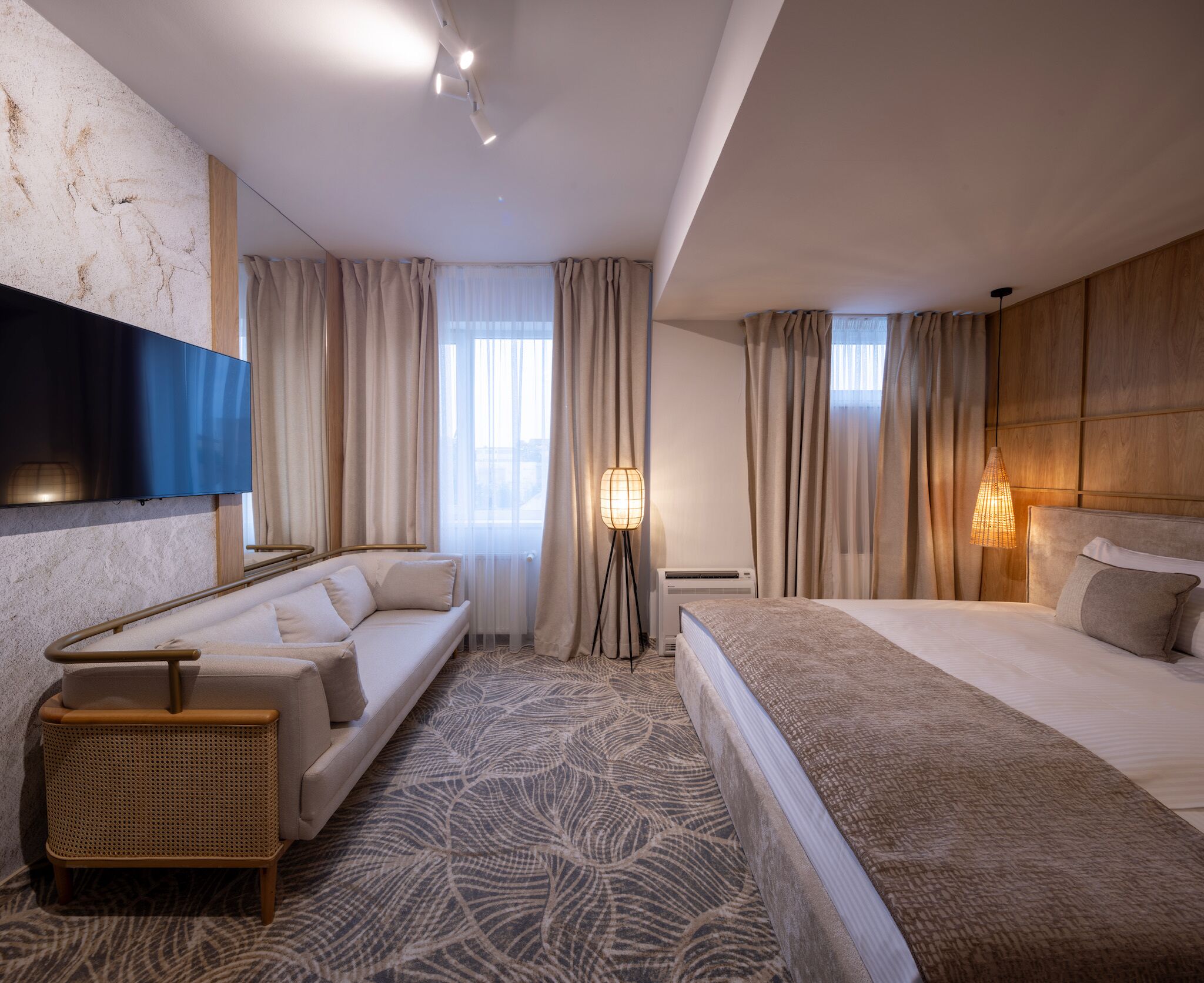A modern hotel room with a sofa, a bed, a flat-screen TV, and a floor lamp.