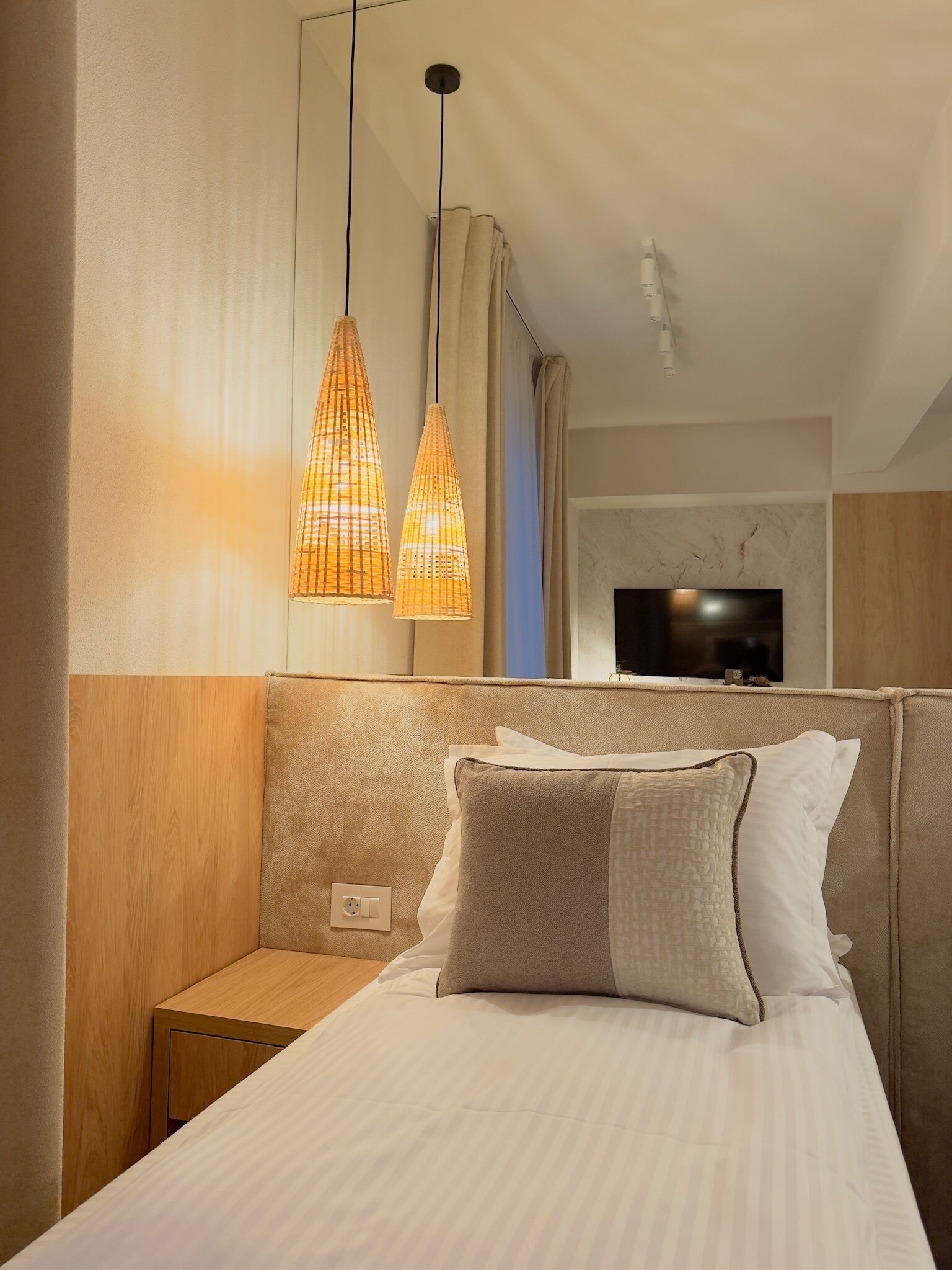A hotel room with a bed, a nightstand, a TV, and a wall-mounted light fixture.