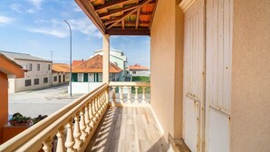 Un balcone con ringhiera in legno, vista sulla strada, e un edificio con tetto in tegole rosse sullo sfondo.