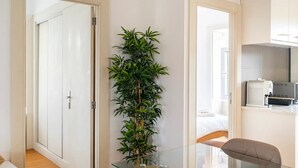 Una camera d'albergo moderna con un tavolo in vetro, una pianta verde di grandi dimensioni e un letto con biancheria bianca.