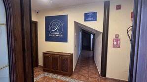 Un pasillo de hotel con un armario de madera, piso de baldosas y señales que indican los números de las habitaciones y los equipos de emergencia.