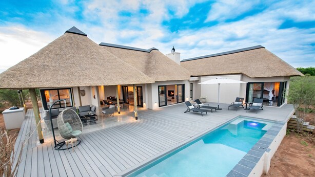 Une villa moderne dotée d’une piscine, d’un espace salon extérieur et d’une structure à toit de chaume.