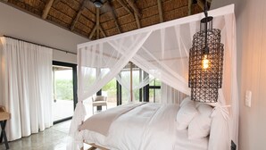 Une chambre à coucher avec un lit à baldaquin, un luminaire suspendu et une vue sur l’extérieur.