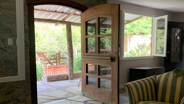 Una habitación con puerta de madera que da a un espacio exterior, un sofá a rayas y una pared de piedra.