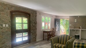Amplia sala de estar con una pared de piedra, una mesa de comedor con sillas, un sofá a rayas y una zona de cocina con pileta y encimera.