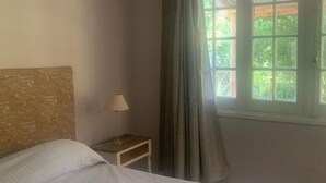 Un dormitorio con cama, mesita de noche, lámpara y ventana con cortinas.