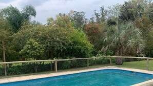 Una piscina rectangular con cerramiento de madera y malla metálica, rodeada de abundante vegetación y árboles.