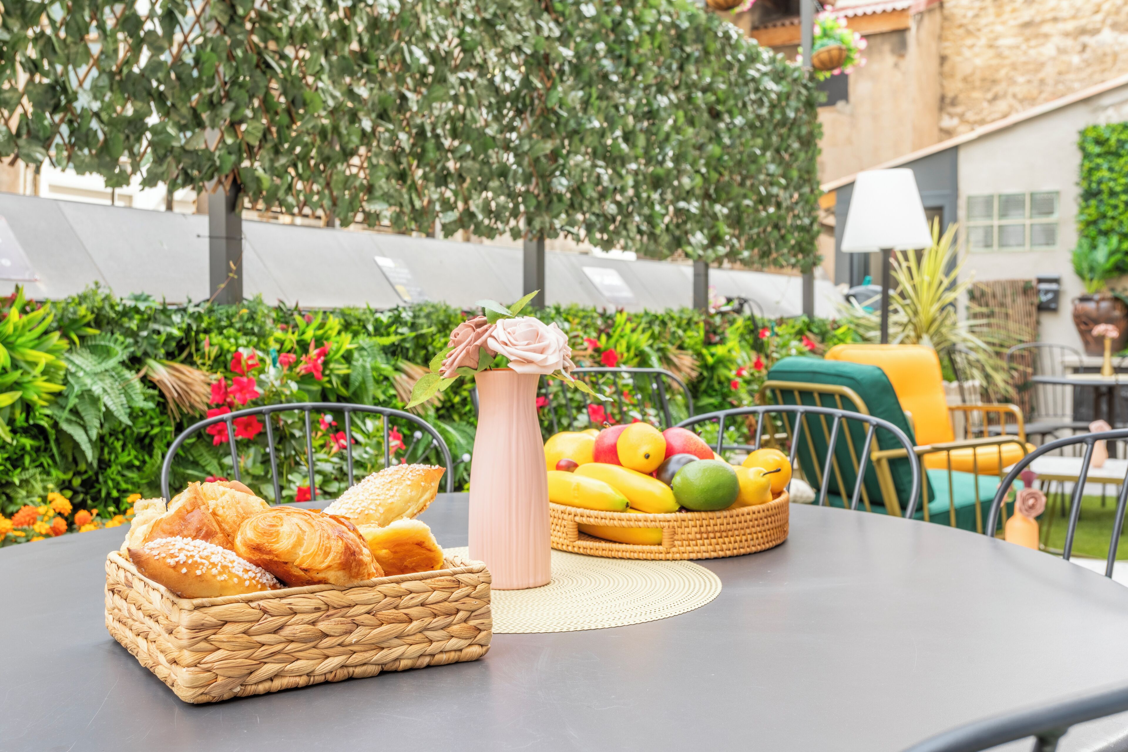 A table with a basket of bread, a vase with flowers, and a basket of fruit.