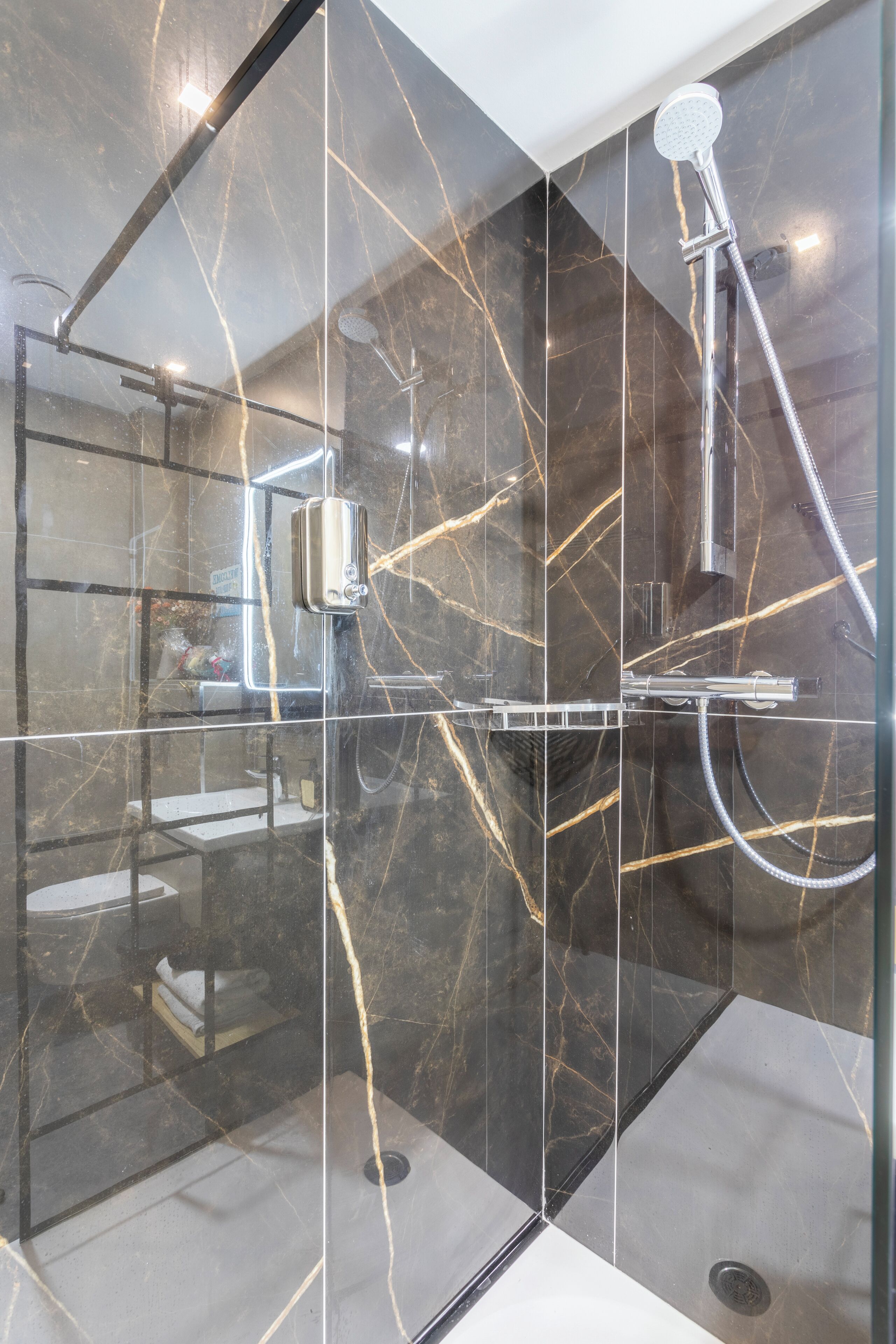 Une salle de bain moderne avec une douche à parois de verre, des murs en marbre et des toilettes apparentes.