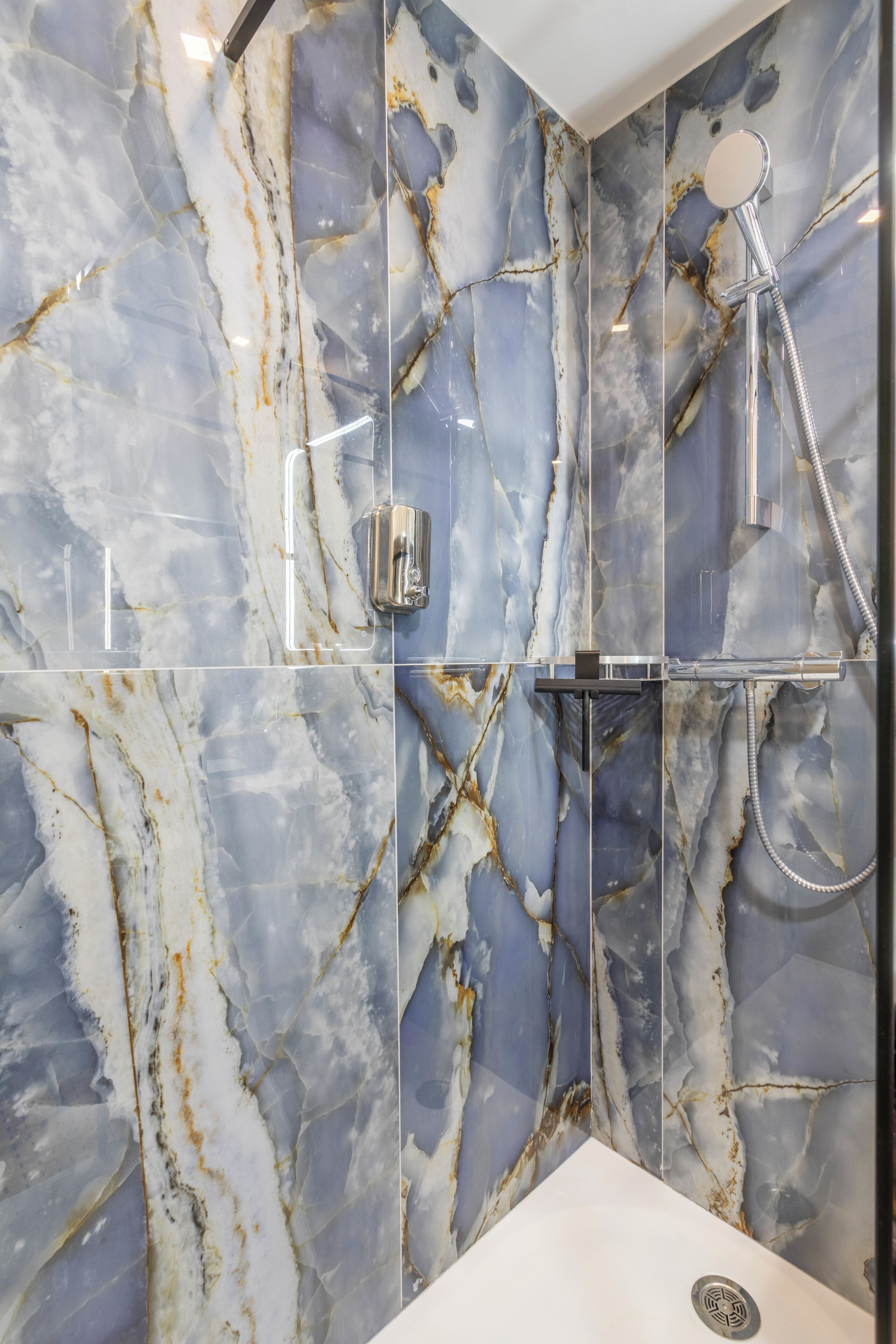 A bathroom with marble walls, a shower, and a sink.