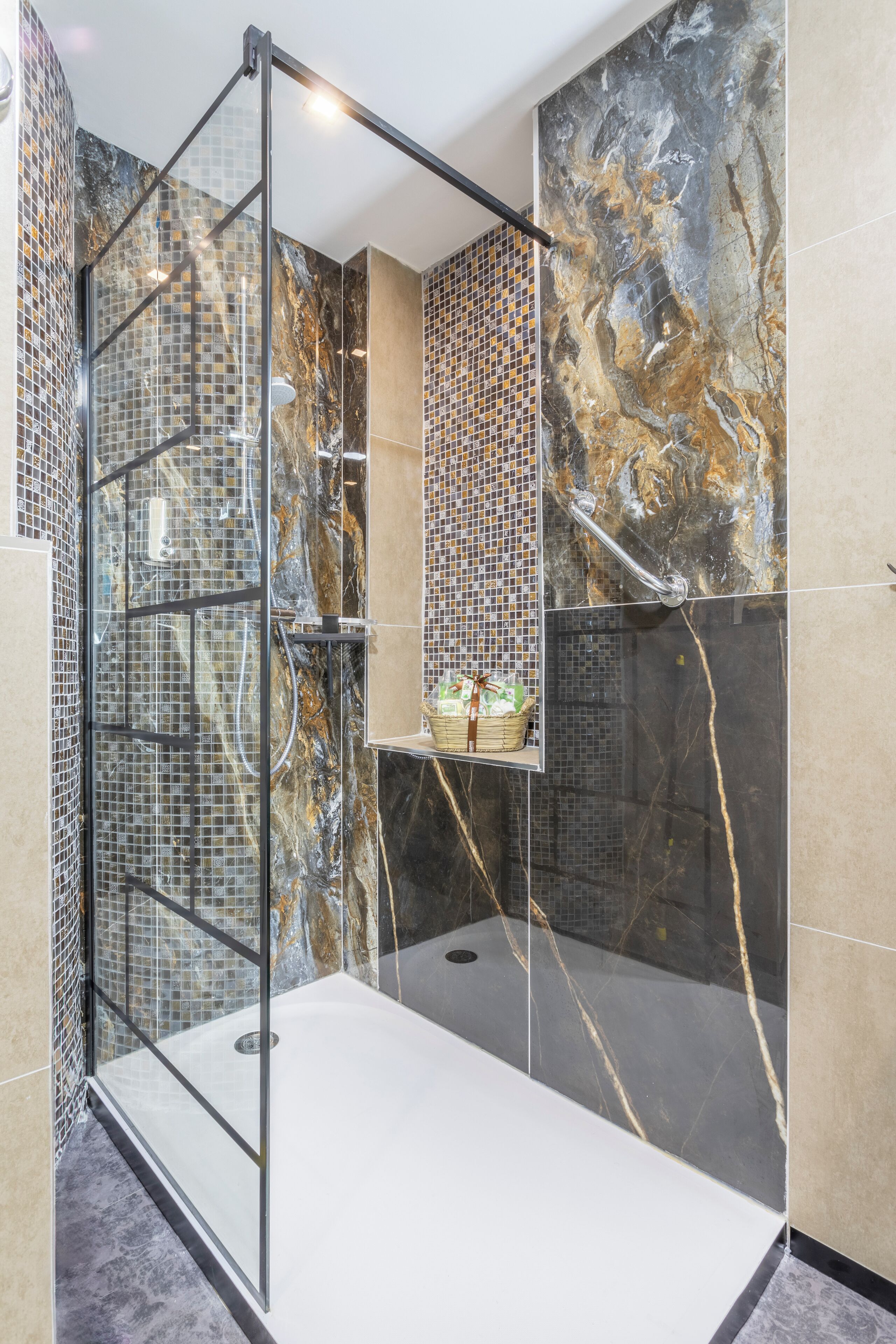 A modern shower enclosure with a glass door, a built-in shelf with toiletries, and a marble wall design.